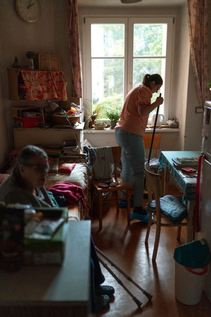 services-03 A caregiver mopping the floor in a cozy Prague apartment, assisting a senior.